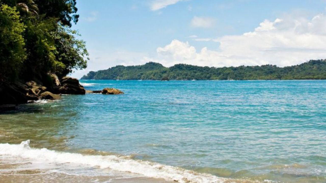  Tropical beach in Tamarindo, Costa Rica, with turquoise water, forested coastline, and palm shadows.