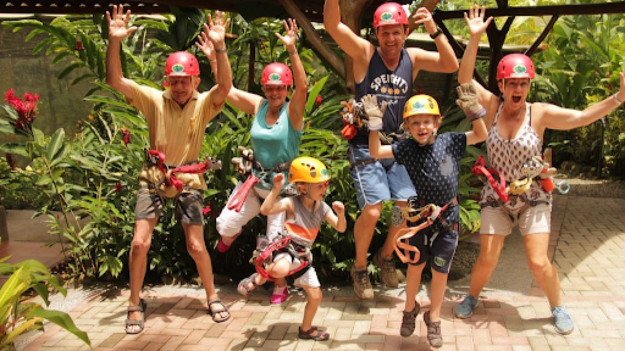 Family jumping together at an outdoor ziplining adventure park surrounded by tropical greenery.